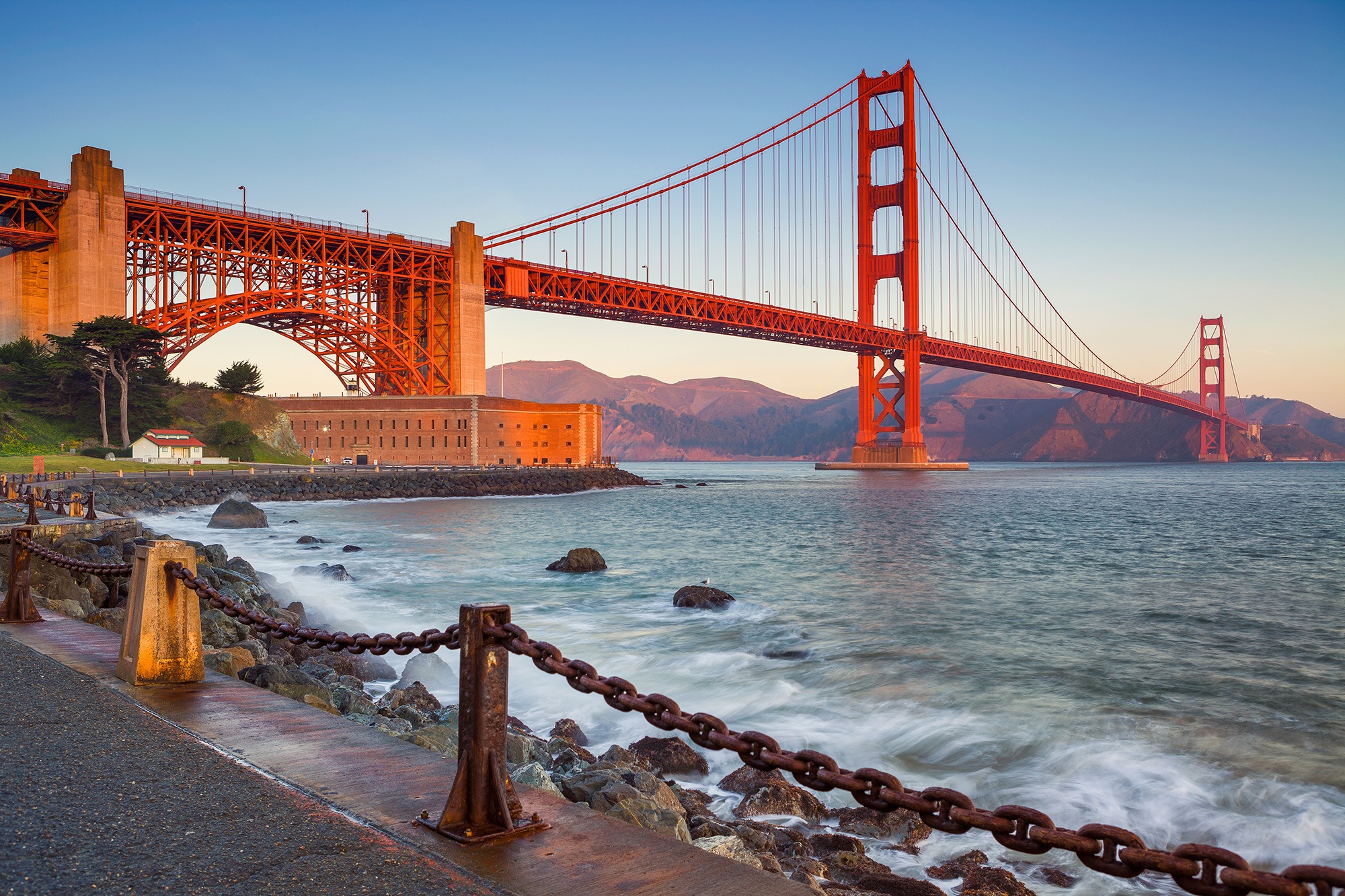 The Golden Gate Bridge illuminated by the sunset looms over the Presidio.
