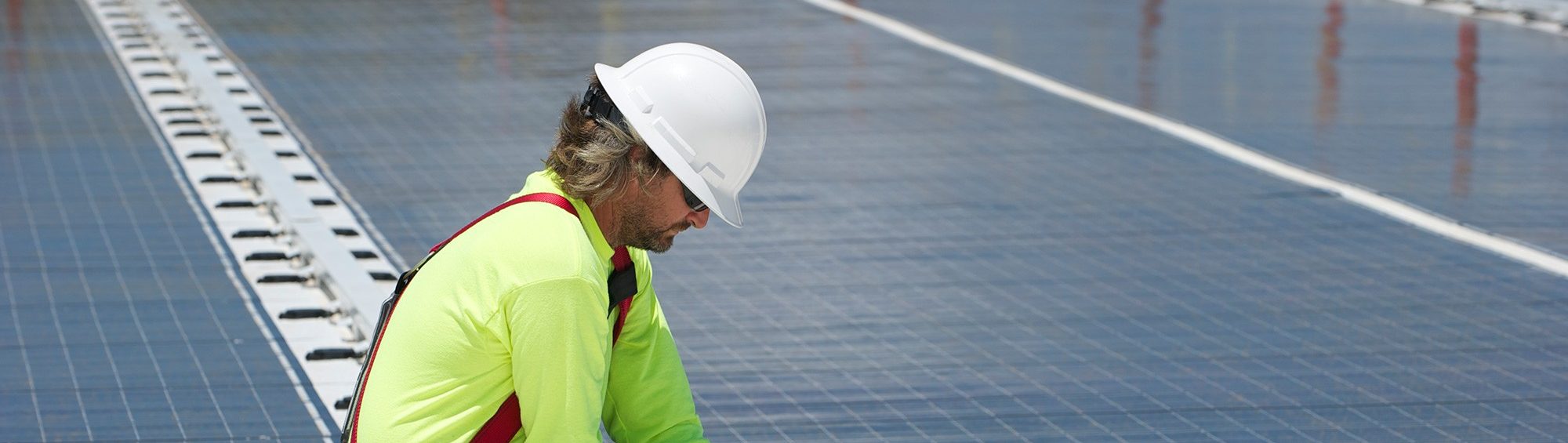 A Coffman engineer wearing a bright yellow shirt and white hardhat works on solar panels for a sustainable design project.
