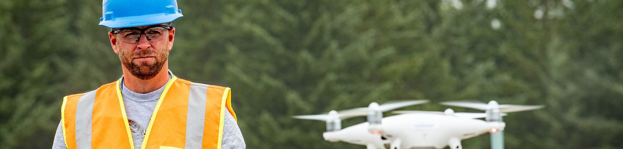 A Coffman engineer wearing a bright orange vest and blue hardhat surveying land on a job site.