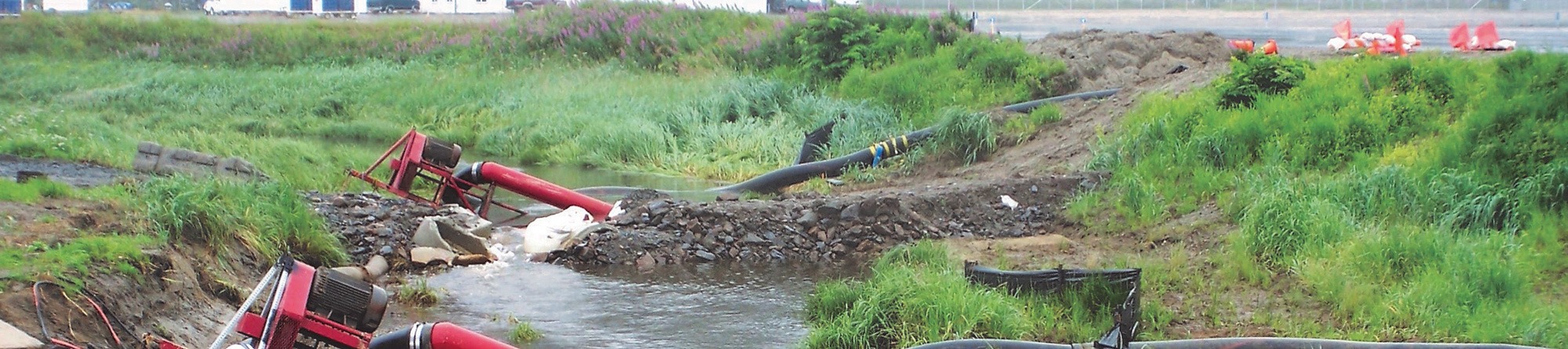 Coffman engineers wearing red uniforms use trenchless technology at a grass-covered job site.