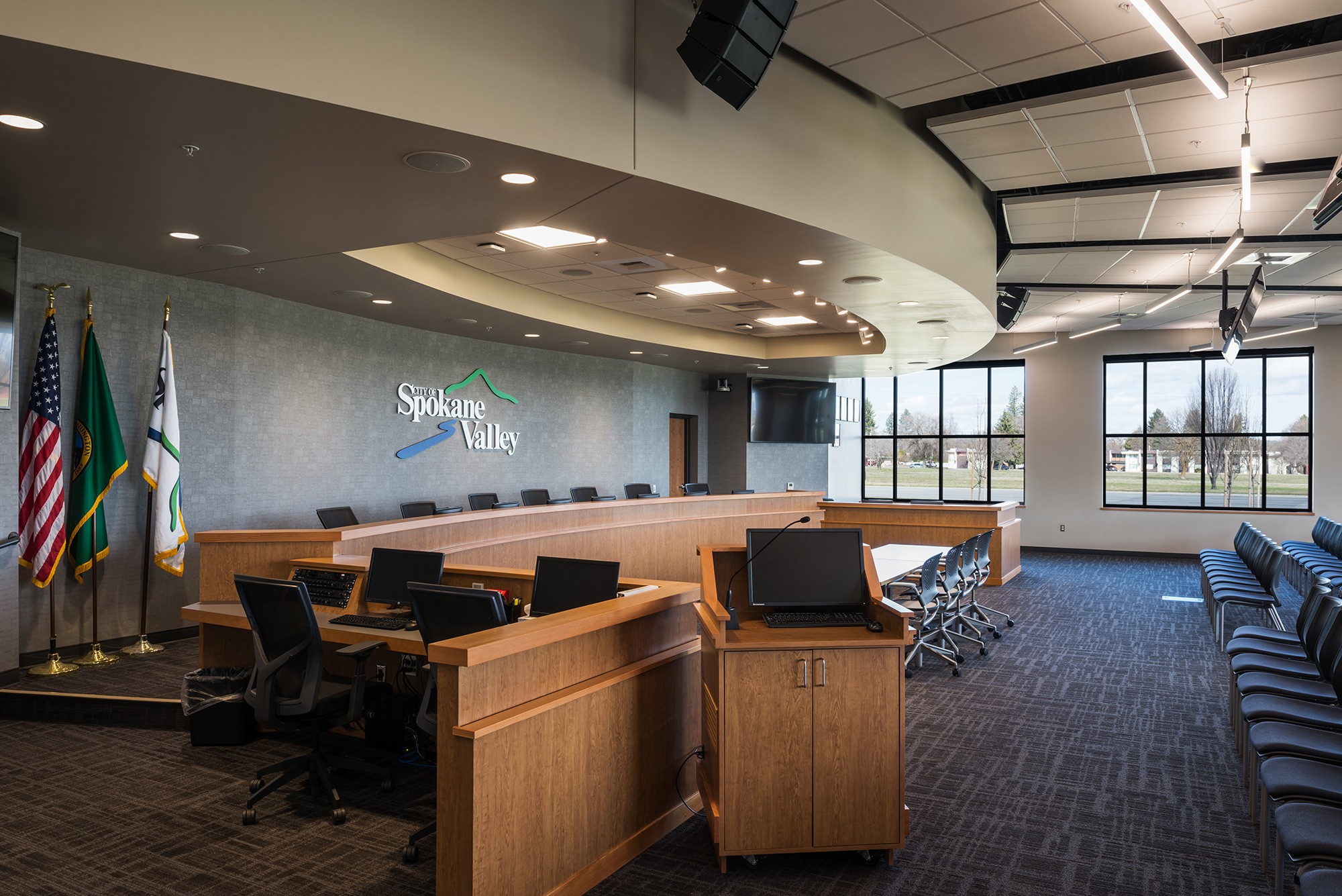 A civic government building room decorated with wood furniture, flags, and chairs.