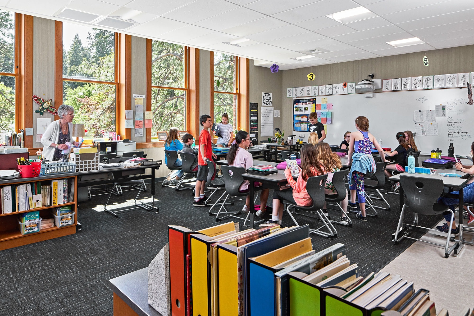 Young children sit at various desks in a colorfully decorated school classroom.