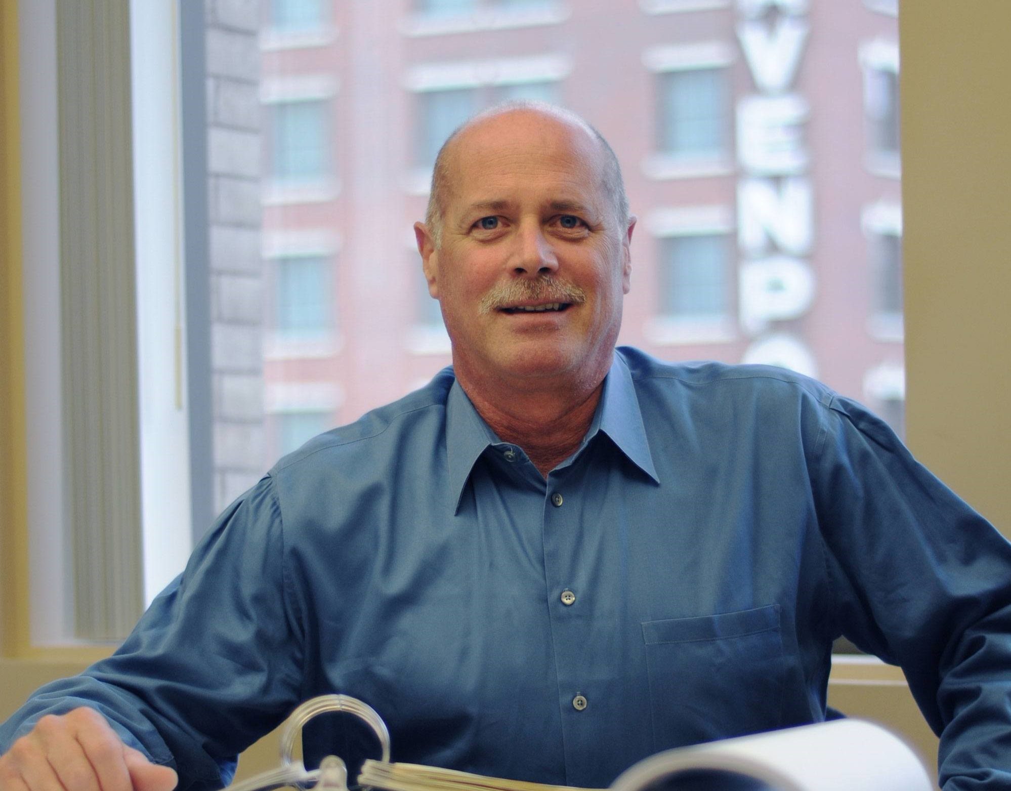 Fire protection engineering VP Bob Libby smiles at a desk in front of a window wearing a blue shirt.