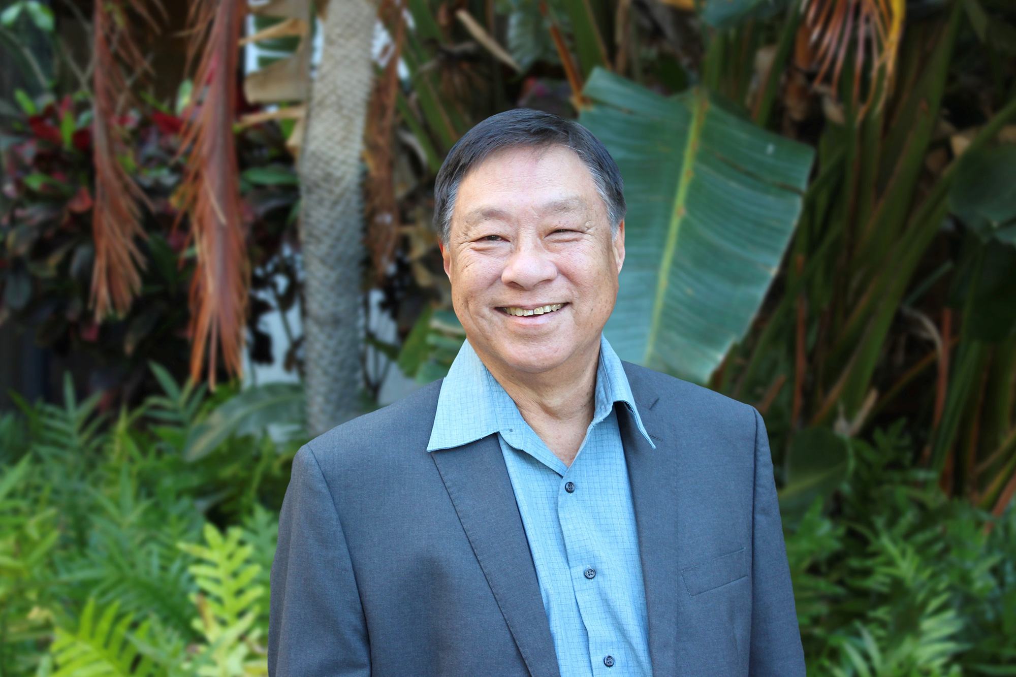 Headshot of man with green foliage in background.